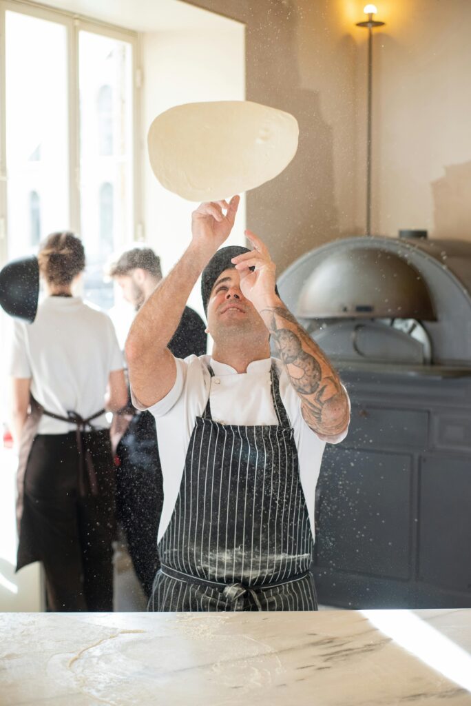 pexels-photo-6605189-6605189-1 A chef in a traditional Portuguese bakery tosses pizza dough with skill, illuminated by natural daylight.